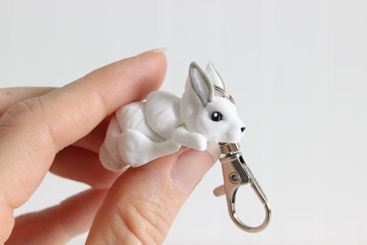 Hand holding 3D-printed white snow rabbit keychain with a silver swivel quick-clip.