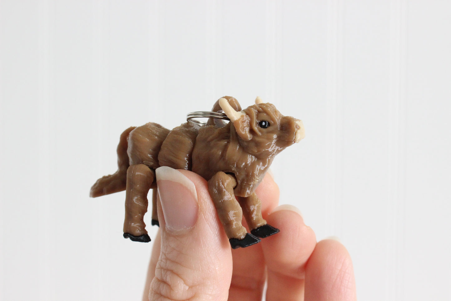 Alternate view of the 3D-printed shaggy brown Highland cow keychain showing its sculpted details and segmented design.
