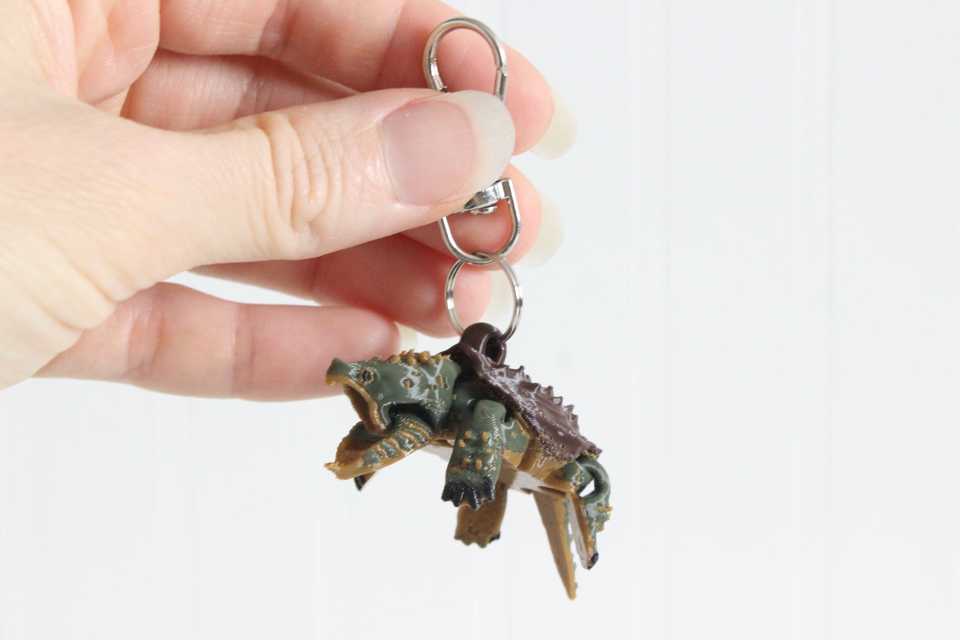 Hand holding a 3D printed alligator snapping turtle keychain showing dark brown ridged shell and articulated legs with swivel quick-clip key ring